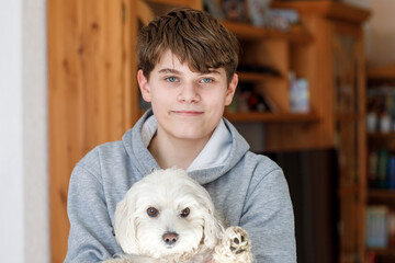 Happy teenager boy and cute maltese puppy together. Handsome child holding his dog at home,...