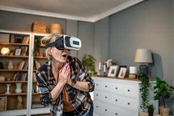 Amazed mature woman wearing vr headset interacting with virtual reality at home