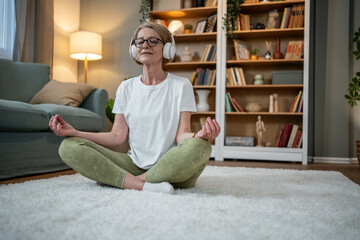 Senior woman meditating with headphones in living room