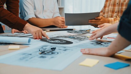 A group of professionals engages in a collaborative discussion over design plans and blueprints laid out on a modern office table, fostering creative teamwork. SACTR