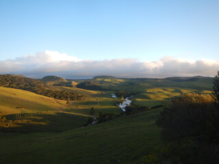 Photograph showing green fields and a river in the late afternoon