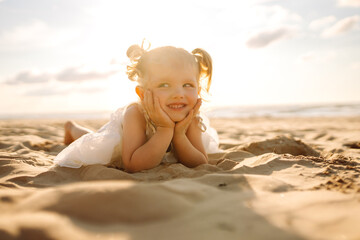 Happy little girl having fun on the beach on a sunny day. Beautiful child spending time together outdoors. Childhood, fun concept.