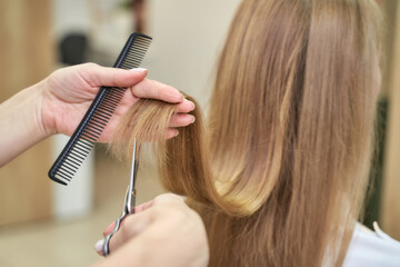 Caucasian female receiving haircut in salon with scissors and comb close up.