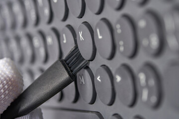 Close up of gloved hand cleaning keyboard with small brush for maintenance and hygiene.