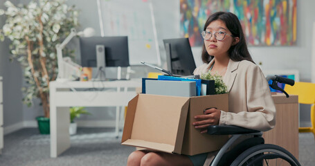 Sad disillusioned disappointed young woman with glasses with sorrow leaves her job in the company, she was fired by disability, illness, wheelchair, injustice of employer, boss, unemployment