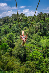 Young girl experience the exhilarating adrenaline rush of swinging high above the breathtaking and stunning greenery of Bali beautiful tropical jungle landscape, Ubud, Indonesia © Dawid