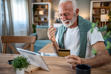 Senior man using tablet and credit card for online shopping at home