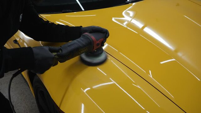 Detailing process of polishing yellow sports car hood surface using orbital polishing machine at car service 4k video. Using abrasive paste for polishing with orbital polisher for remove scratches.