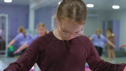 Young kids actively engaged in a fitness workout session, focusing on exercises one glasses concentrating on her movement while others in the background participate in gym activities