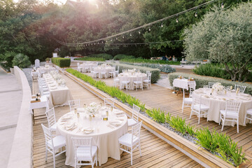 Festive served tables on a wooden flooring in the garden among green bushes