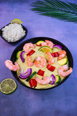 A mouthwatering dish of tiger prawns, fresh vegetables and lime wedges served on a black plate against a tropical backdrop.