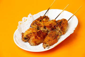 Crispy Grilled Chicken Wings on Skewers served in plate isolated on orange background side view of hong kong food