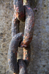 Close-up of a rusted chain resting on a cement background, highlighting the texture and weathered details of both the chain and the surface