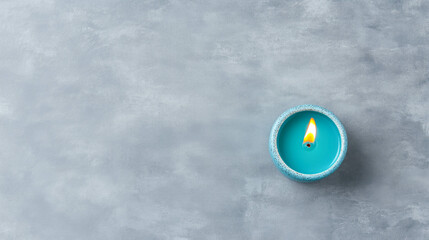 Blue candle with bright flame on gray textured surface for relaxation and calm ambiance
