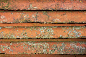Old, weathered red roof tiles stacked with visible margins, showing spots of mold and moss growth