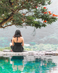 Mujer sentada de espaldas bajo un árbol, rodeada de naturaleza y muros rústicos
