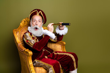 Conceptual portrait of a mature man in vintage costume seated on a gold chair with a telescope...