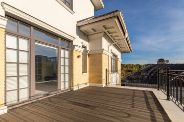 A luxurious two-storey house made of light brick against a blue sky. The sunlit terrace is a...