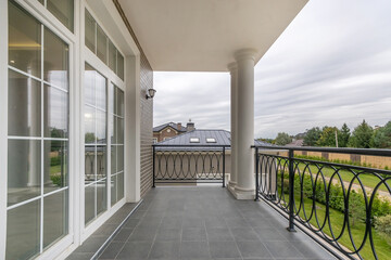 The balcony of a luxurious brick country house with a view of a green lawn. Balcony with columns...