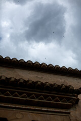 Dramatic sky with birds flying above a traditional building rooftop
