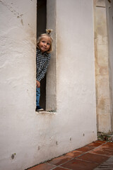 A young child peeking out from a small window, playfully tilting their head