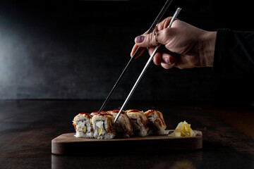 A hand elegantly grips chopsticks, preparing to savor delicious sushi rolls adorned with a savory...