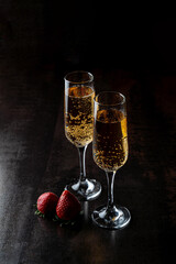 In the warm glow of a restaurant, two sparkling glasses of bubbly champagne stand elegantly beside fresh strawberries, inviting an atmosphere of celebration and indulgence