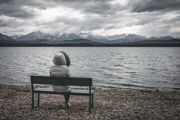 Fototapeta premium Woman in jacket sitting on bench on the shore of the lake