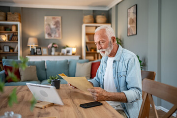Senior man reading important documents at home using tablet