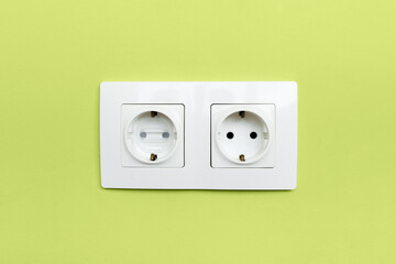 two white electrical outlet one of which with safety plug for children on green wall