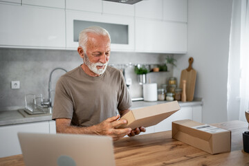 Happy senior man unpacking cardboard box in kitchen at home