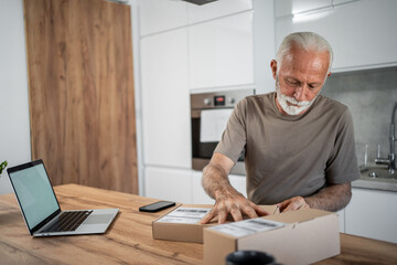 Senior man opening package at home in his kitchen