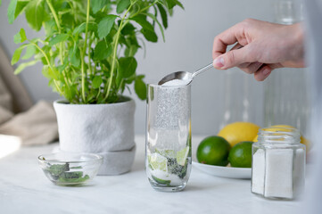Crafted homemade mojito cocktail drink making process, home kitchen with fresh ingredients, lime, mint, sugar. Pouring sugar in glass with lime and mint