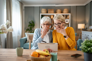 Two senior women sharing a moment of surprise while using a digital tablet at home