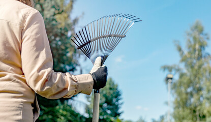 Gardener holding rake near tree and gardening in garden. Blue sky background.