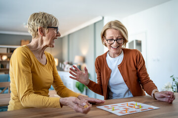 Two senior women playing board games and having fun at home