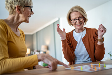 Two senior women playing board games at home having fun