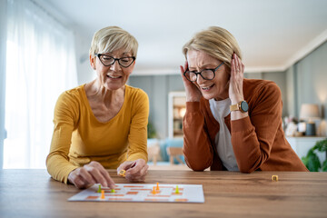 Two senior women playing board game at home