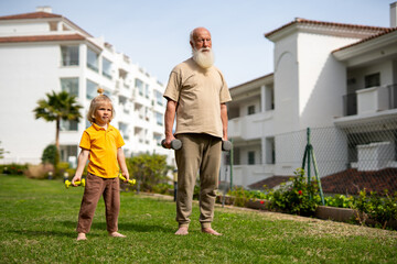 Grandfather and grandson exercising with dumbbells together in the garden