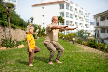 Obraz premium Grandfather and grandson practicing squats together outdoors