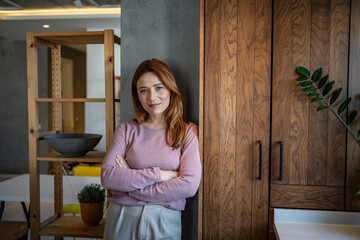 Smiling woman leaning against wall with crossed arms in modern apartment