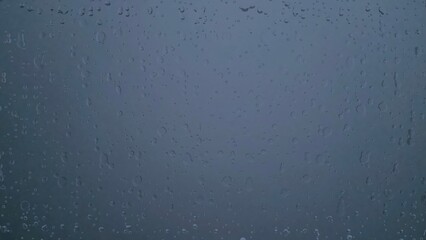 Raindrops on a glass window with a moody, dark blue background, creating a serene and melancholic atmosphere.