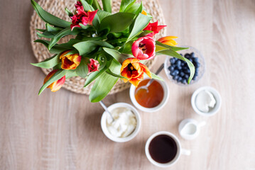 A bouquet of tulips in a glass vase in the living room and breakfast with coffee, cottage cheese and berries