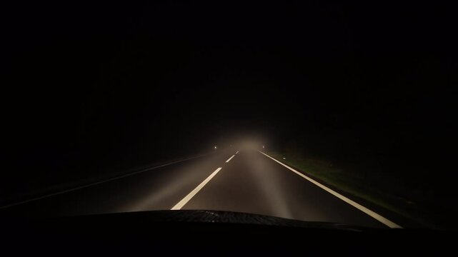 Driving in bad conditions on a foggy road at night. Front car windshield and white beam of lights. Winter weather concept, real time footage with evening lights. Nothing to see on the streets.