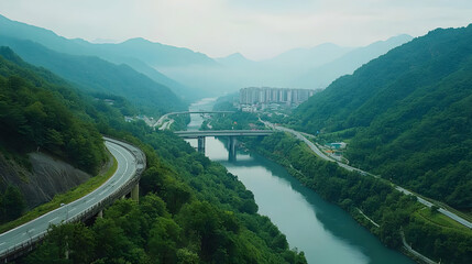 Aerial View Of Mountainous Landscape With River Bridge And Road Surrounded By Greenery Under Overcast Sky
