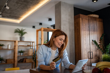 Smiling woman making online payment using digital tablet and credit card at home