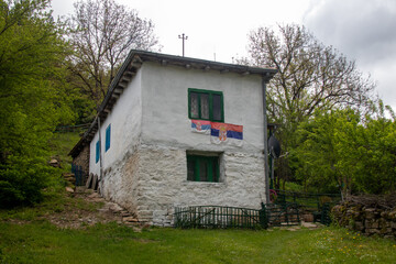 Charming stone house with green windows in a serene landscape featuring a flag in a rural region