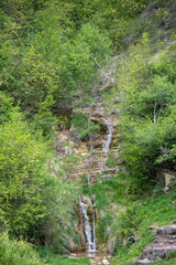 Waterfall cascading down green hillside surrounded by lush vegetation in a tranquil natural setting