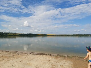 boy 3 years old running on beach, to summer lake, forest distant, fields, calm, white clouds, blue sky, sand, reflection, 
summer, vacation, walk, tourist