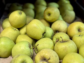 A mound of large green coloured apples in boxes is displayed in the window of the supermarket's vegetable stand, demonstrating organic, vegetarian and healthy food. Close-up